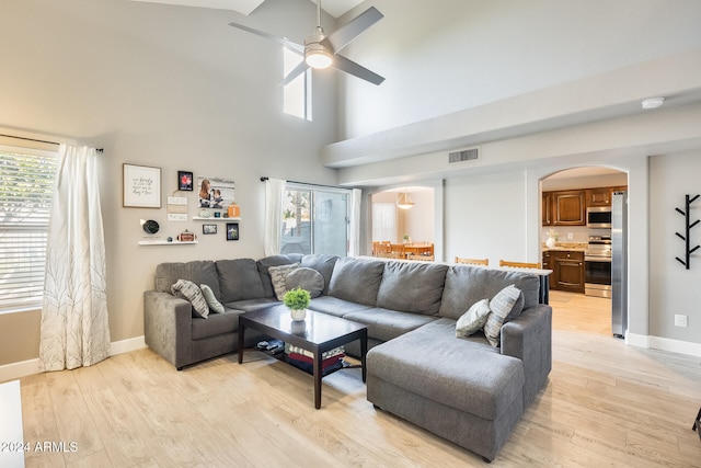 living room featuring ceiling fan, a high ceiling, and light wood-type flooring