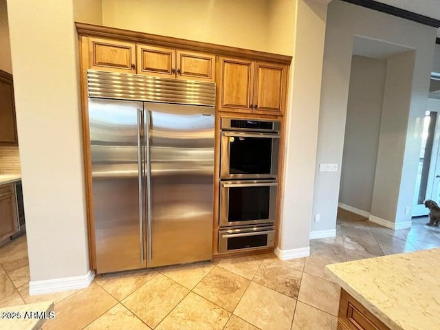 42023 N Bridlewood Way, Anthem, AZ 85086 - kitchen featuring appliances with stainless steel finishes, brown cabinets, a warming drawer, light stone counters, and baseboards