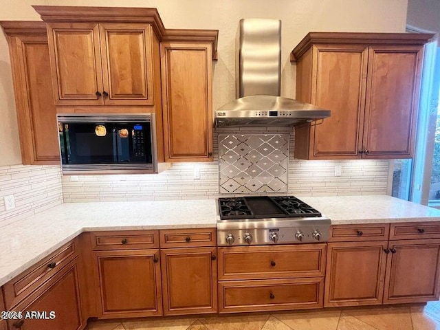 42023 N Bridlewood Way, Anthem, AZ 85086 - kitchen featuring stainless steel appliances, wall chimney exhaust hood, brown cabinetry, tasteful backsplash, and light stone countertops