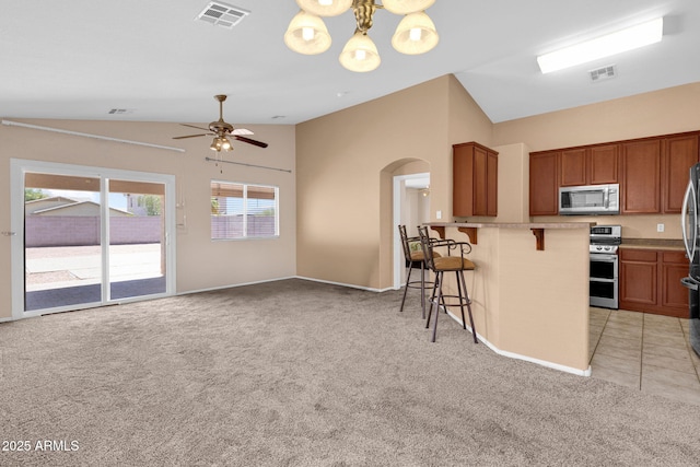 1623 E Maplewood Ave, Buckeye, AZ 85326 - kitchen featuring stainless steel appliances, lofted ceiling, light colored carpet, arched walkways, and a kitchen breakfast bar