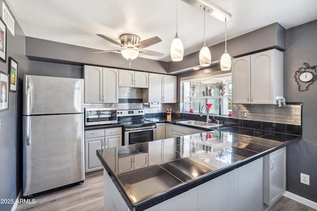 kitchen featuring a sink, light wood-type flooring, a textured wall, decorative backsplash, and appliances with stainless steel finishes