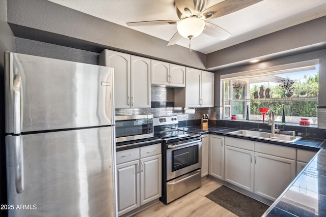 kitchen with a sink, light wood-type flooring, backsplash, a ceiling fan, and appliances with stainless steel finishes