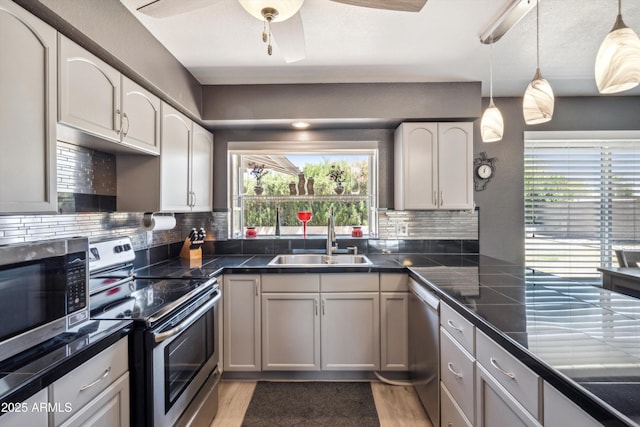 kitchen with light wood-style flooring, a sink, stainless steel appliances, ceiling fan, and tasteful backsplash