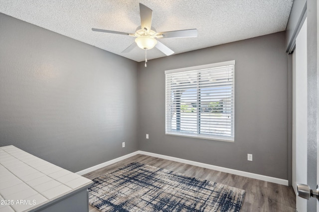 empty room with a textured ceiling, baseboards, a ceiling fan, and wood finished floors