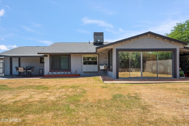 back of house featuring a sink, roof with shingles, stucco siding, a lawn, and central AC unit