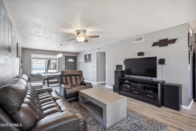 living room with a ceiling fan, light wood-type flooring, visible vents, and a textured ceiling