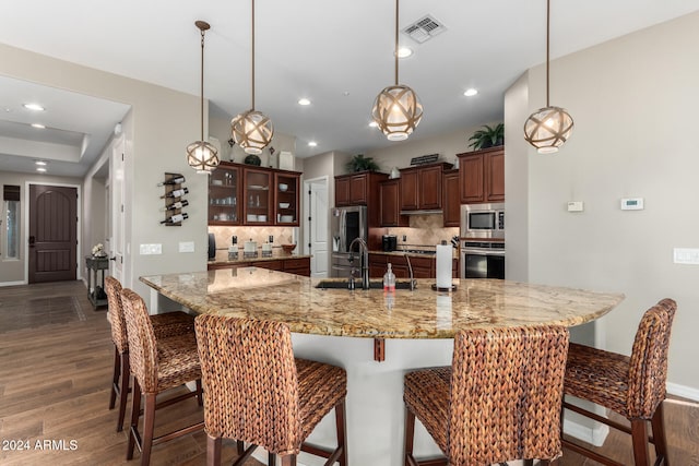 kitchen featuring a large island with sink, dark wood-type flooring, appliances with stainless steel finishes, and tasteful backsplash