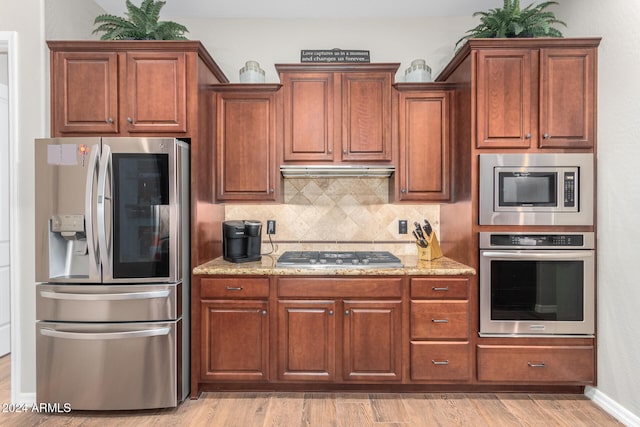 kitchen with appliances with stainless steel finishes, light stone countertops, tasteful backsplash, and light wood-type flooring