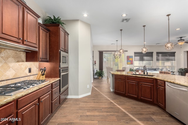 kitchen featuring appliances with stainless steel finishes, sink, decorative light fixtures, light stone counters, and dark hardwood / wood-style floors