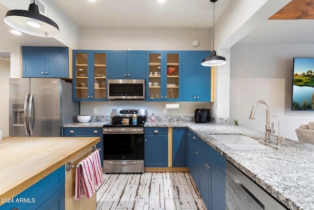 kitchen featuring light stone countertops, appliances with stainless steel finishes, sink, blue cabinetry, and hanging light fixtures