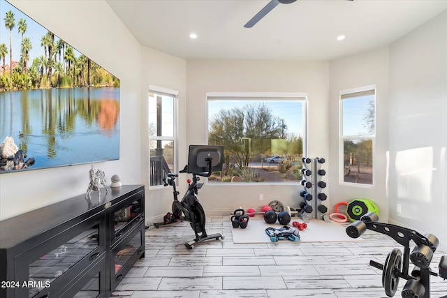 exercise room with ceiling fan, a water view, and light hardwood / wood-style flooring