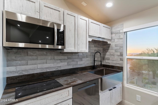 kitchen featuring white cabinetry, sink, stainless steel appliances, backsplash, and vaulted ceiling