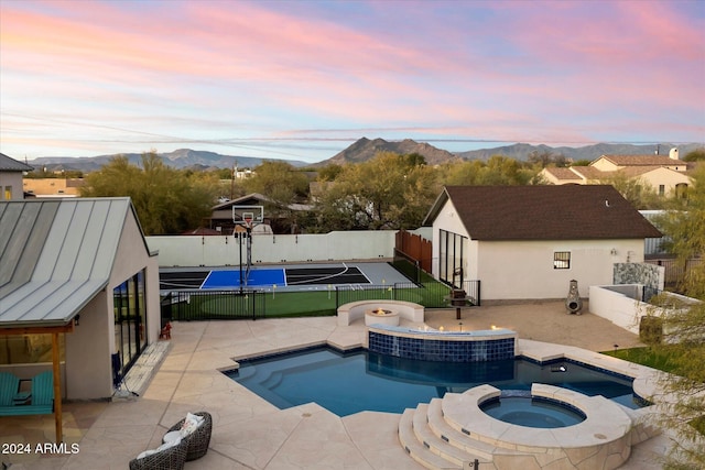 pool at dusk with a mountain view, a patio, and an in ground hot tub