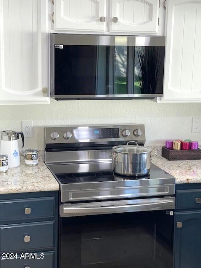 kitchen with white cabinetry, blue cabinets, light stone counters, and stainless steel electric range