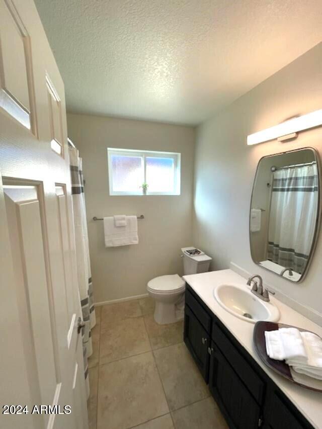 bathroom featuring toilet, a textured ceiling, vanity, a shower with shower curtain, and tile patterned flooring