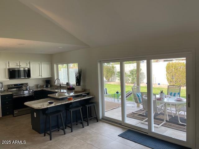 kitchen featuring lofted ceiling, sink, appliances with stainless steel finishes, white cabinets, and a kitchen bar