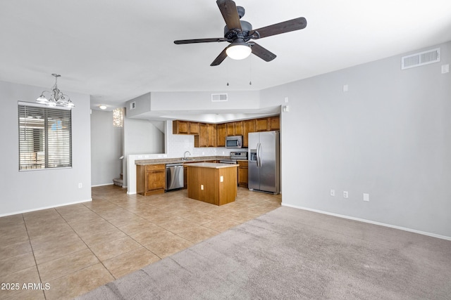 kitchen with ceiling fan with notable chandelier, stainless steel appliances, a center island, light tile patterned flooring, and decorative light fixtures