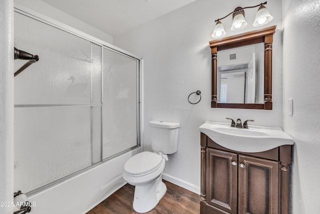 full bathroom featuring baseboards, bath / shower combo with glass door, toilet, wood finished floors, and vanity