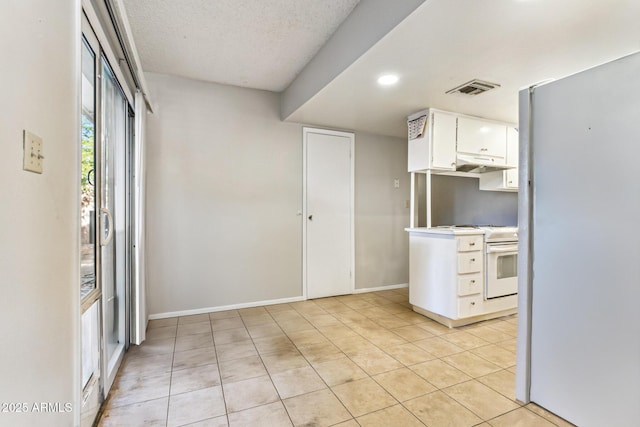 kitchen with white appliances, light tile patterned floors, a textured ceiling, and white cabinets