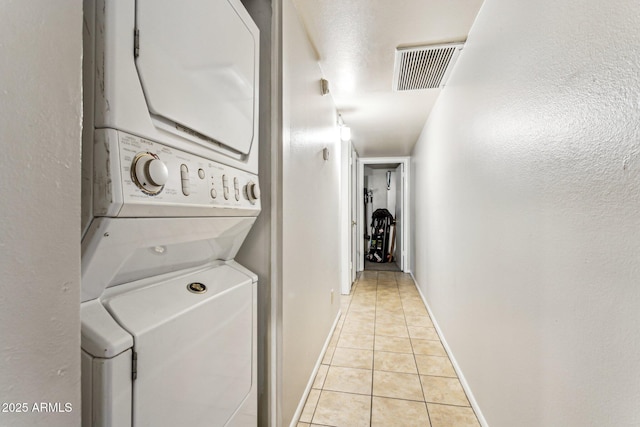 laundry area with stacked washer / drying machine and light tile patterned floors