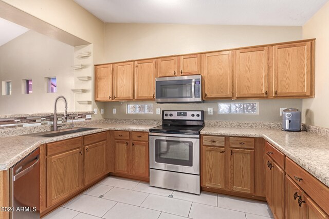 kitchen with kitchen peninsula, appliances with stainless steel finishes, vaulted ceiling, sink, and light tile patterned floors