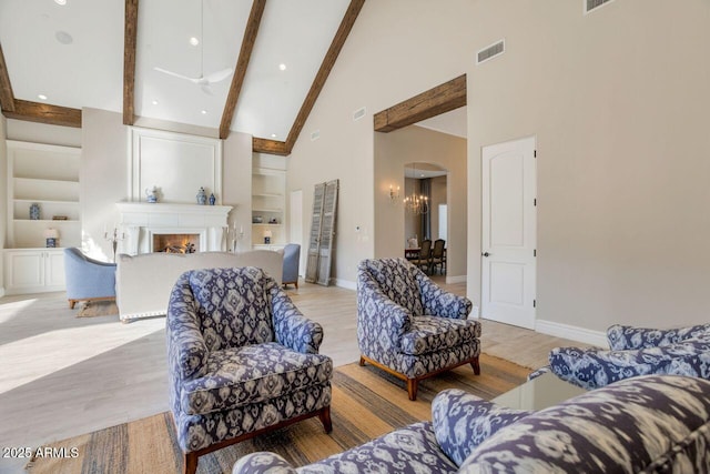 living room featuring light hardwood / wood-style floors, high vaulted ceiling, beam ceiling, and built in shelves