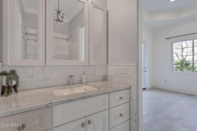 bathroom with a chandelier, decorative backsplash, hardwood / wood-style flooring, vanity, and crown molding