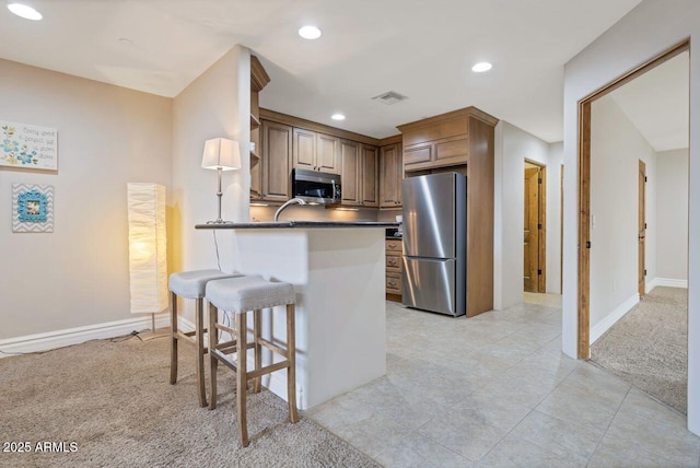 kitchen with stainless steel appliances, kitchen peninsula, light carpet, and a breakfast bar area