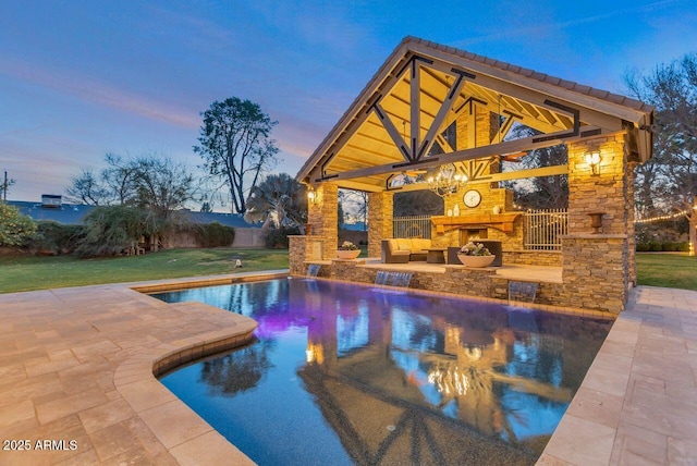 pool at dusk with a gazebo, a yard, a patio, and an outdoor stone fireplace