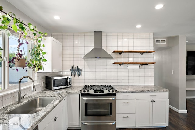 kitchen featuring stainless steel appliances, wall chimney range hood, a sink, white cabinets, and tasteful backsplash