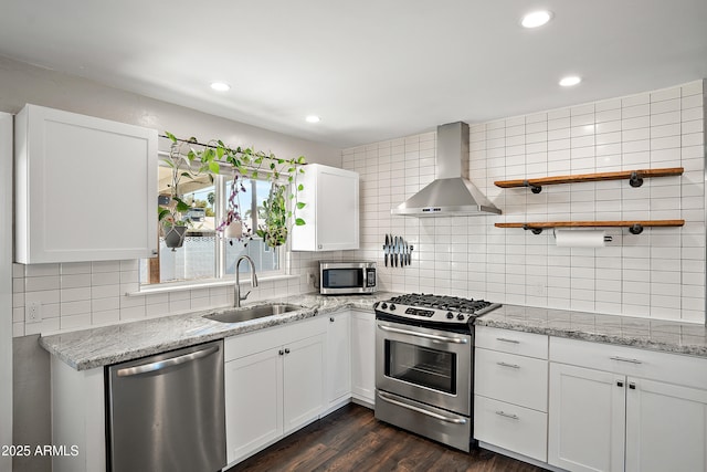 kitchen featuring appliances with stainless steel finishes, a sink, wall chimney exhaust hood, decorative backsplash, and white cabinets