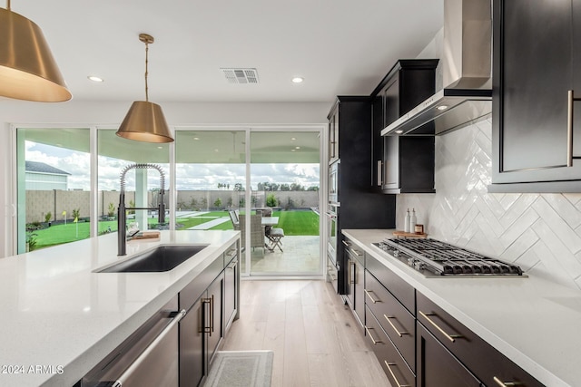 kitchen featuring sink, wall chimney exhaust hood, hanging light fixtures, backsplash, and appliances with stainless steel finishes