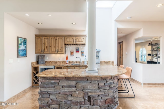 kitchen featuring ceiling fan, a breakfast bar, sink, light stone countertops, and kitchen peninsula