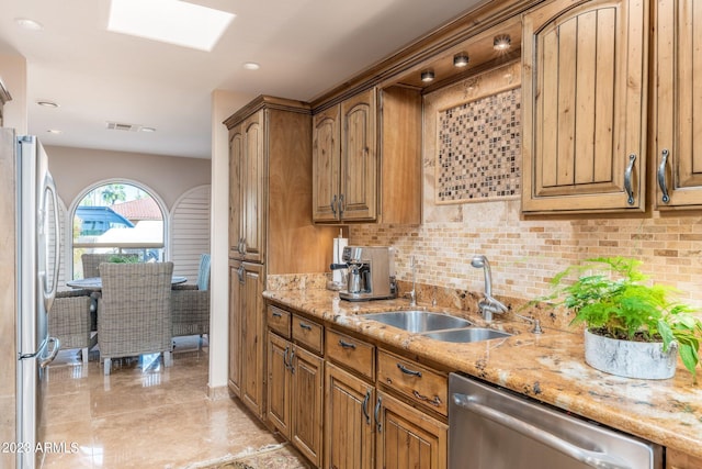 kitchen featuring a skylight, tasteful backsplash, sink, light stone counters, and stainless steel appliances