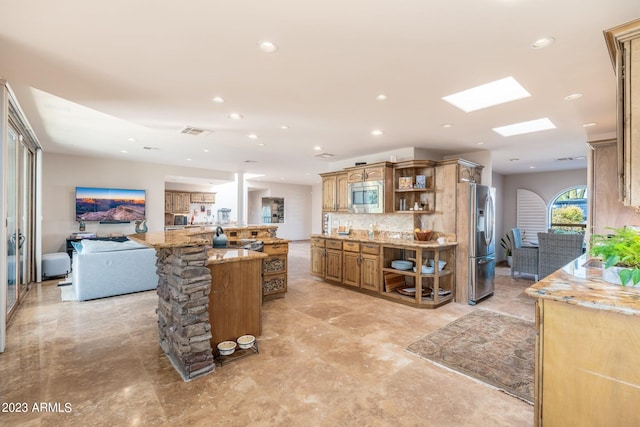 kitchen with decorative backsplash, a skylight, a kitchen island, light stone counters, and stainless steel appliances