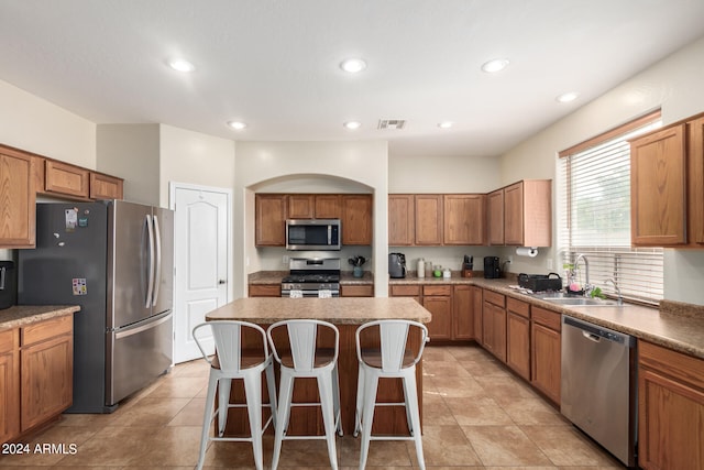 kitchen with a kitchen island, stainless steel appliances, sink, light tile patterned flooring, and a breakfast bar area