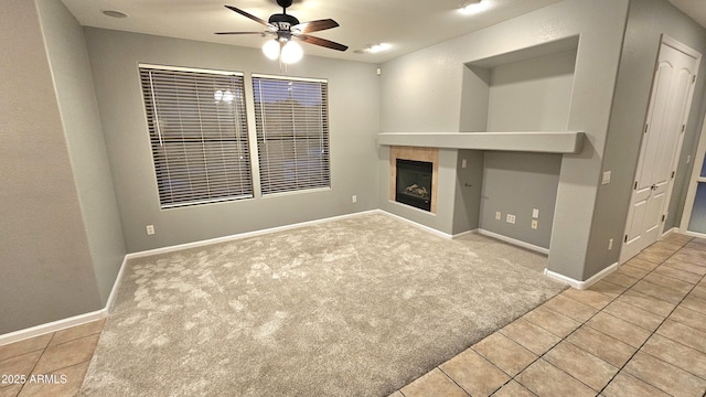 unfurnished living room with ceiling fan, light colored carpet, and a tile fireplace