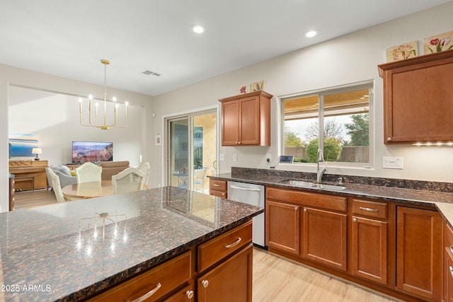 kitchen with dishwasher, sink, an inviting chandelier, dark stone countertops, and light hardwood / wood-style floors