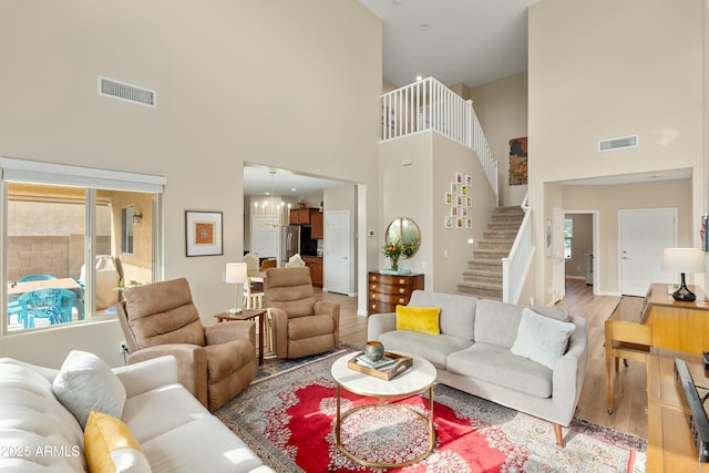 living room with an inviting chandelier, a towering ceiling, and light hardwood / wood-style flooring