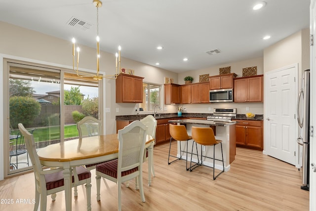 kitchen with hanging light fixtures, an inviting chandelier, plenty of natural light, a kitchen island, and appliances with stainless steel finishes