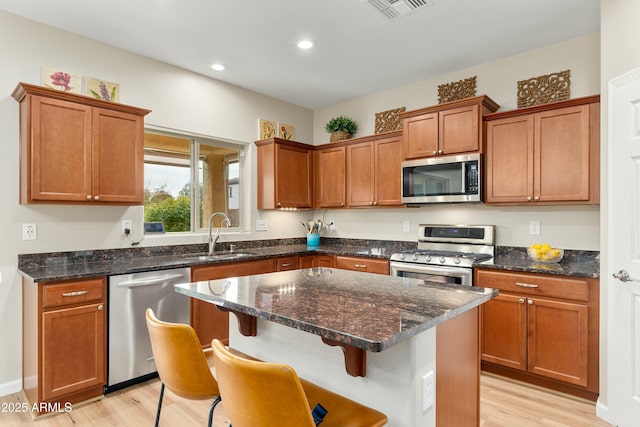 kitchen featuring sink, a breakfast bar area, dark stone countertops, light hardwood / wood-style floors, and stainless steel appliances