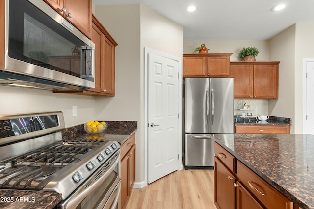 kitchen featuring dark stone countertops, light wood-type flooring, and appliances with stainless steel finishes