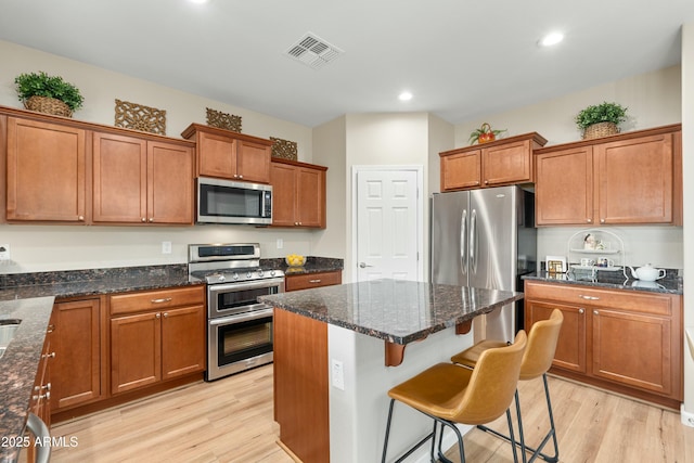 kitchen with a kitchen breakfast bar, light wood-type flooring, stainless steel appliances, and dark stone counters