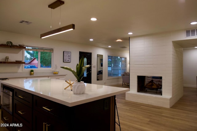 kitchen with pendant lighting, a kitchen island, a breakfast bar area, light hardwood / wood-style flooring, and a fireplace