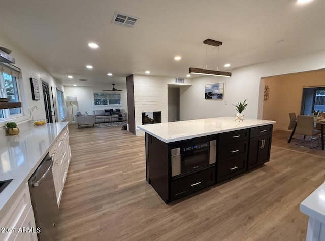 kitchen featuring pendant lighting, white cabinets, a multi sided fireplace, a kitchen island, and appliances with stainless steel finishes