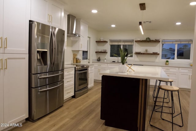 kitchen with wall chimney exhaust hood, light hardwood / wood-style floors, stainless steel appliances, hanging light fixtures, and white cabinetry