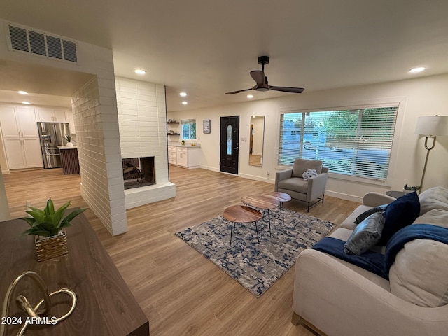 living room with a brick fireplace, light hardwood / wood-style floors, and ceiling fan