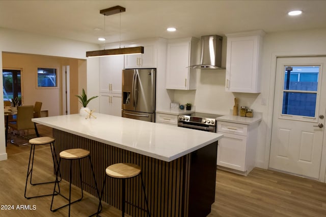 kitchen with wall chimney exhaust hood, light hardwood / wood-style floors, hanging light fixtures, appliances with stainless steel finishes, and white cabinetry