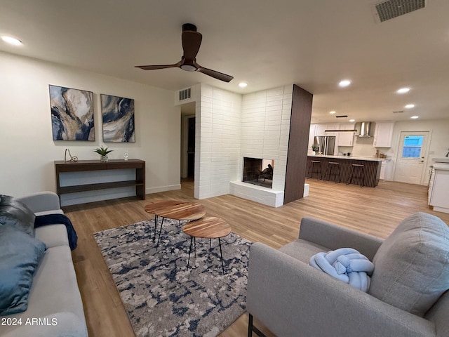 living room with a fireplace, ceiling fan, and light hardwood / wood-style flooring