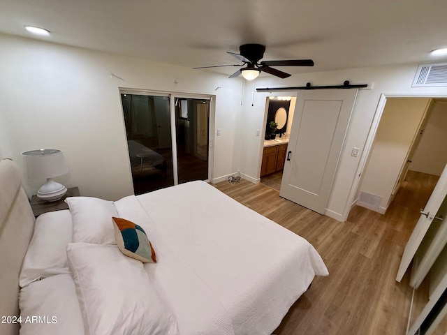 bedroom with ceiling fan, light hardwood / wood-style flooring, connected bathroom, and a barn door